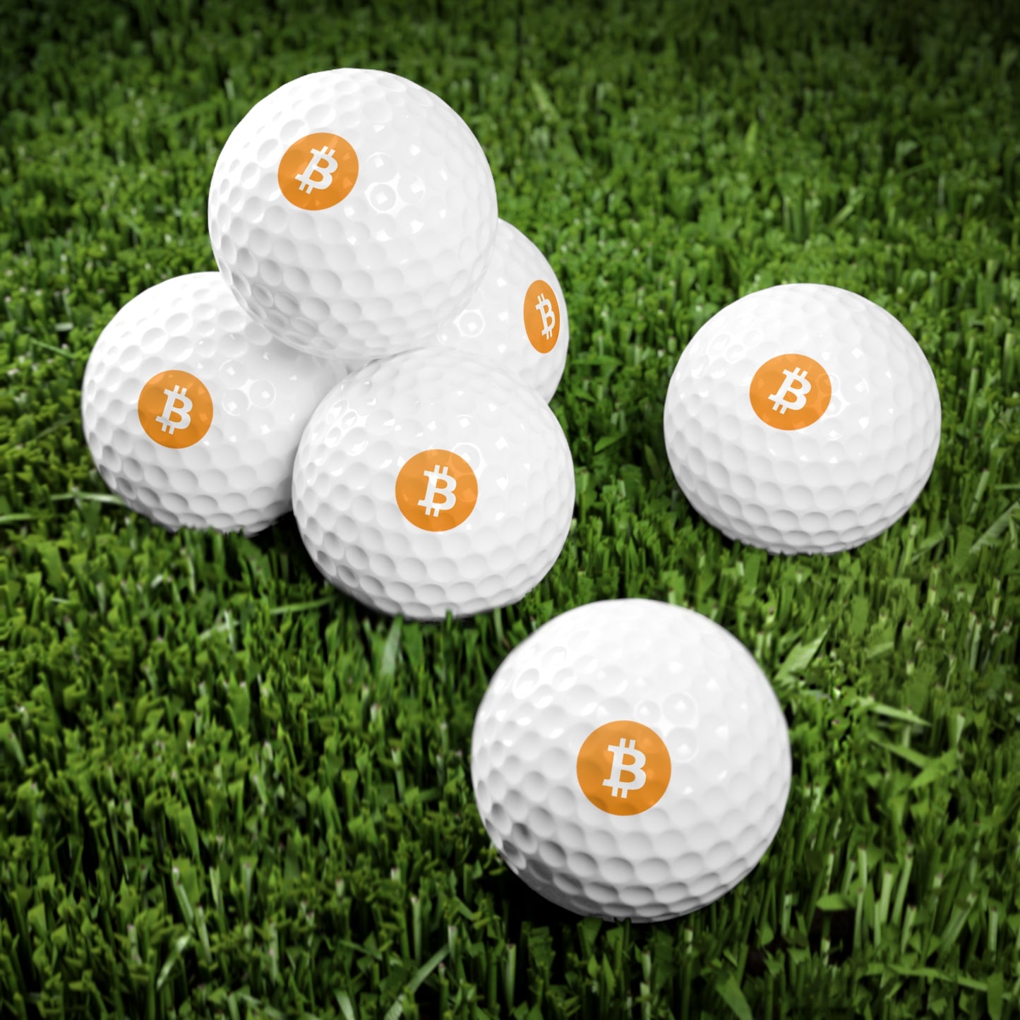 White golf balls with orange Bitcoin ₿ logos on green grass.
